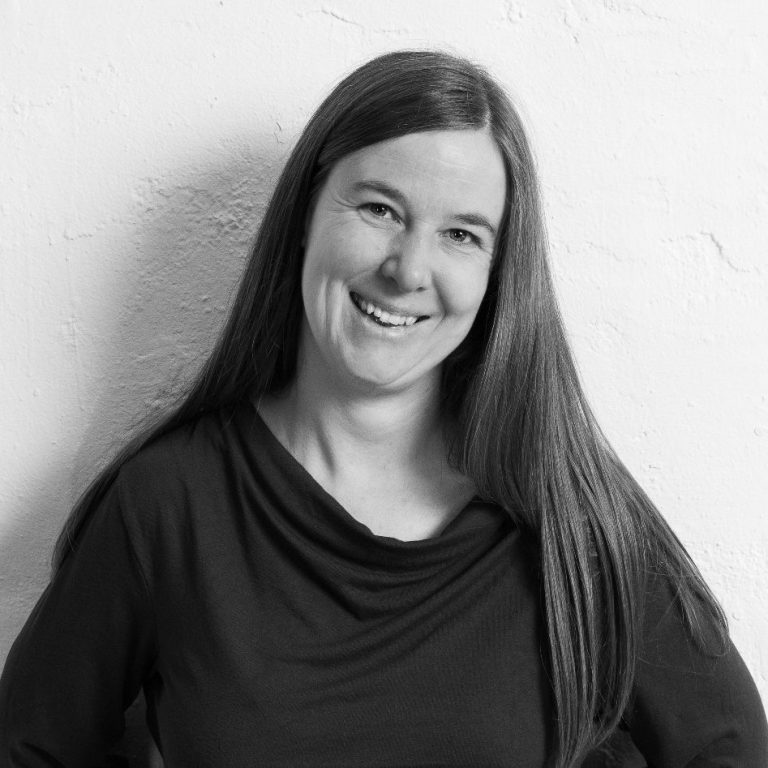 Rebecca Schott mit langen Haaren und einem schwarzen Oberteil lächelt.