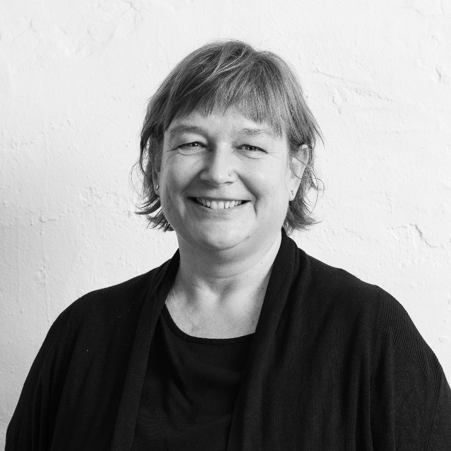 Miriam Schulz mit kurzem, braunem Haar, lächelnd in schwarzer Kleidung vor heller Wand.