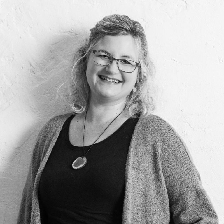 Christine Münch Schulsozialarbeiterin Christine Münch lächelnd mit Brille, die eine graue Strickjacke trägt, steht vor einer weißen Wand.