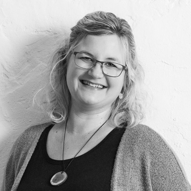 Schwarz-Weiß-Foto von Christine Münch, Schulsozialarbeiterin mit blonden Haaren in einem lässigen, Pullover, lächelt vor weißer Wand.