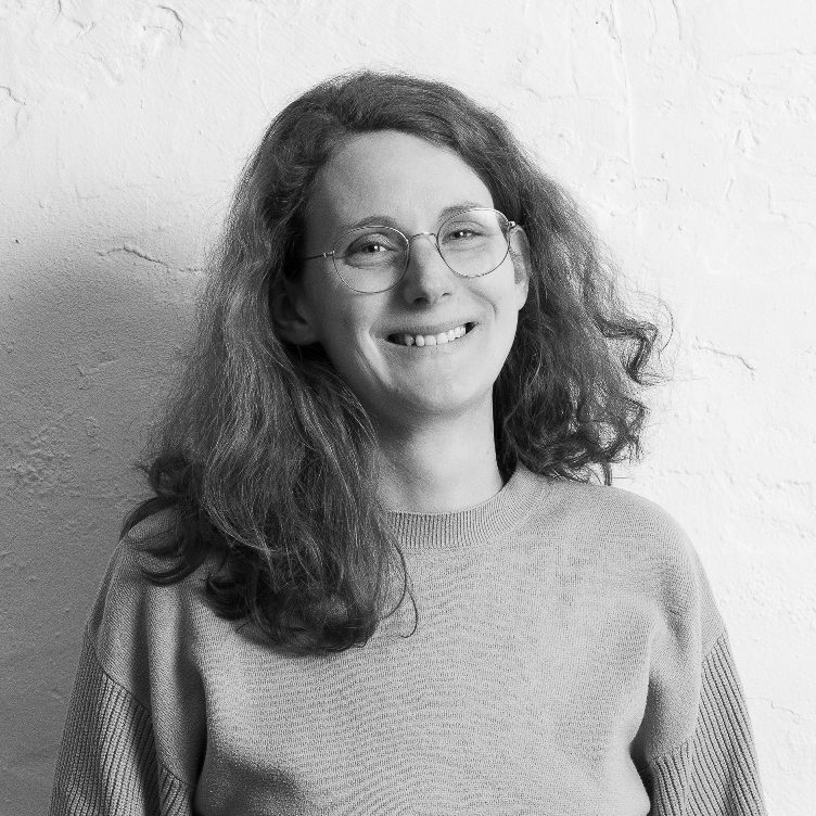 Elisabeth Lammers mit lockigem Haar und Brille, trägt einen grauen Pullover.