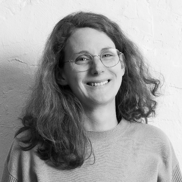 Elisabeth Lammers Elisabeth Lammers mit lockigem Haar und Brille, lächelt vor einer hellen Wand.