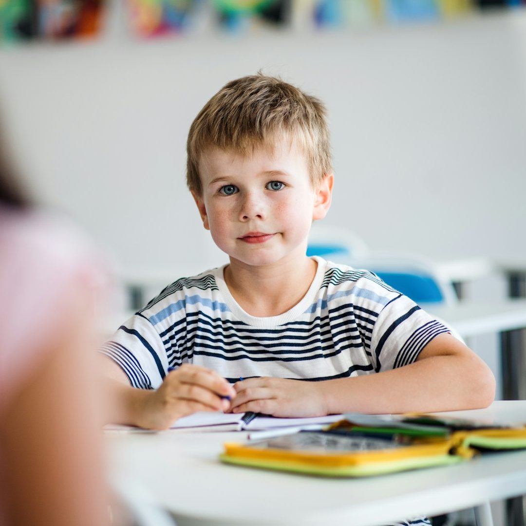 Ein kleines Mädchen mit blonden Haaren, das lachend beim Malen am Tisch sitzt.