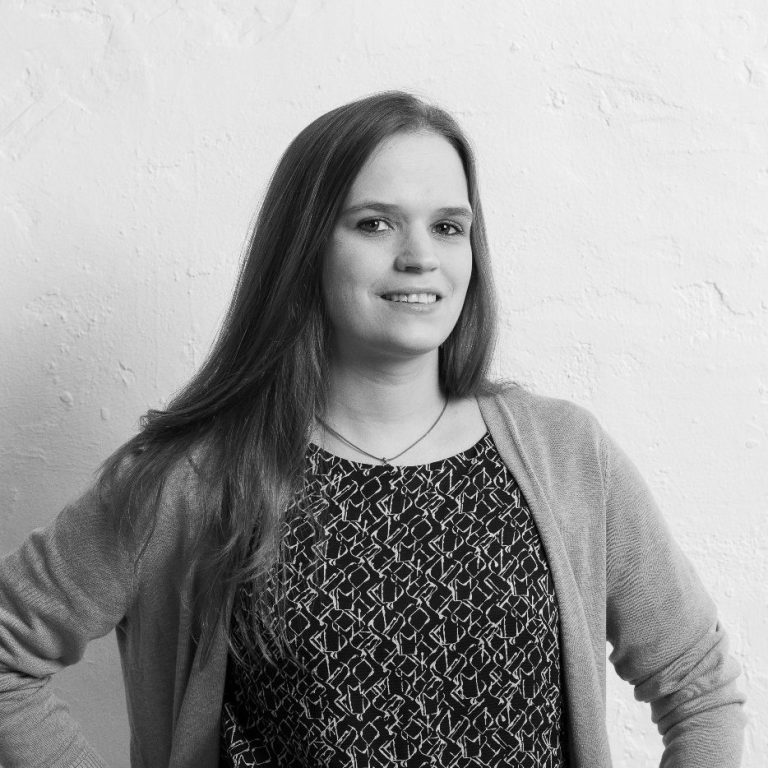 Leonie Lange mit langen Haaren steht mit den Händen in die Hüften gestützt vor einer hellen Wand.