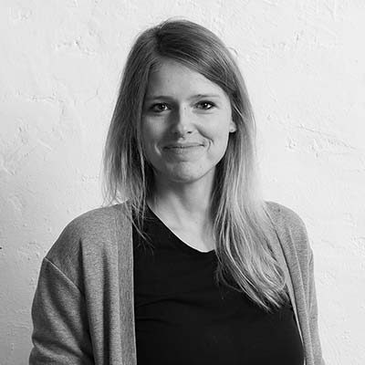 Laura Thiel Laura Thiel lächelnd mit langen Haaren, die in einem hellen Raum steht.