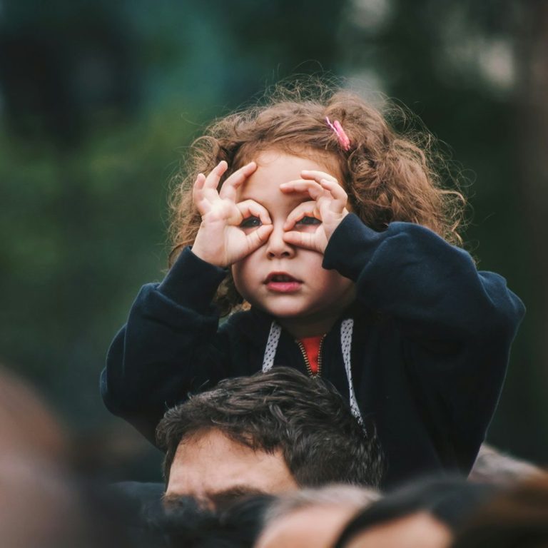 Kinder im Blick Ein kleines Mädchen sitzt auf den Schultern eines Erwachsenen und formt mit den Händen ein Fernrohr.