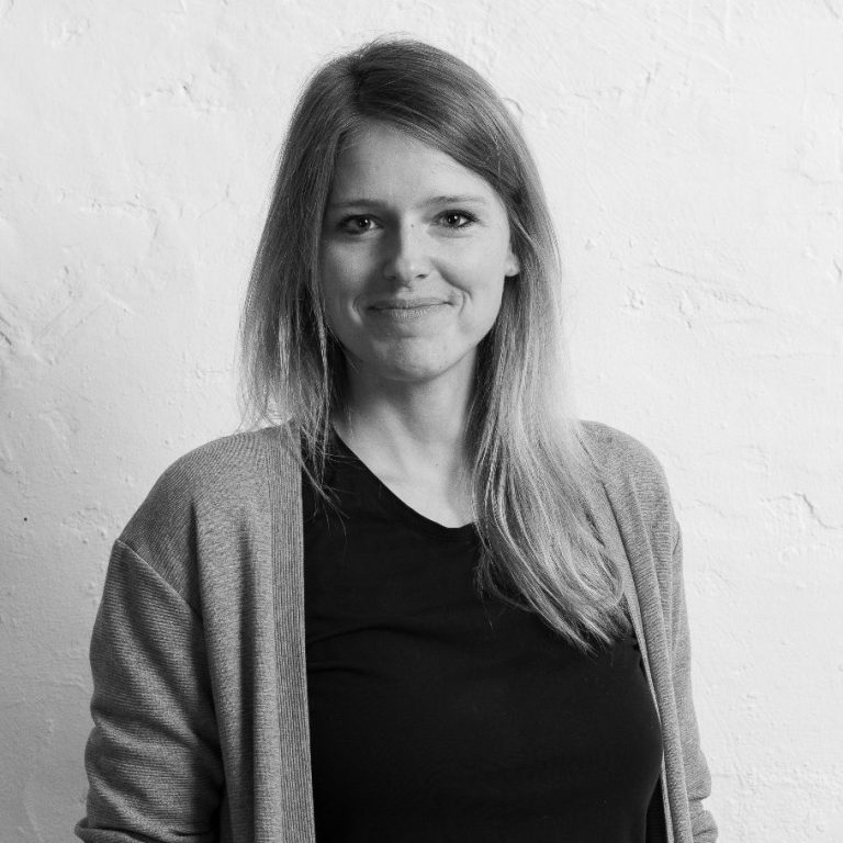 Laura Thiel lächelnd mit langen Haaren, die in einem hellen Raum steht.