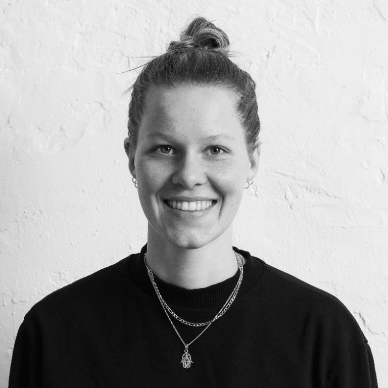 Pia Loddenkemper lächelnd in schwarzem Oberteil vor einer hellen Wand.