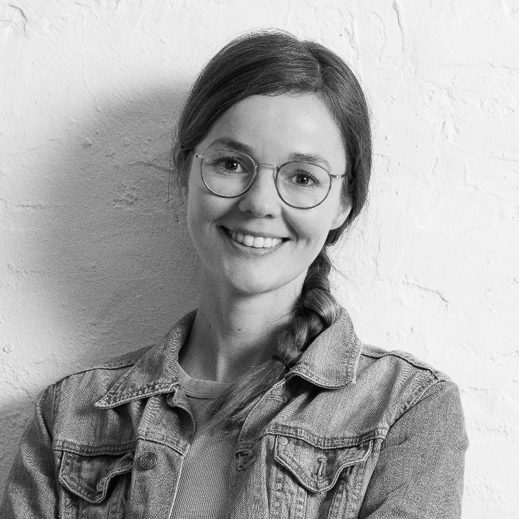 Lisa Bokeloh Lisa Bokeloh mit Brille und Zopf, trägt eine Jeansjacke vor einer hellen Wand.