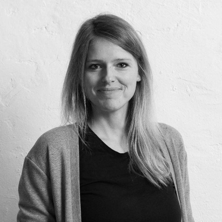 Laura Thiel mit langen Haaren, die in einem hellen Raum lächelt, trägt einen grauen Cardigan.