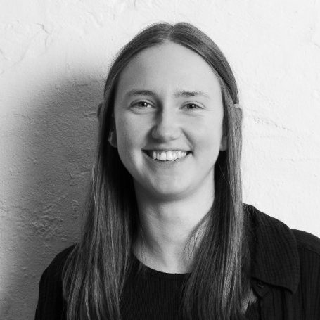 Jana Wilper mit langen Haaren vor einer hellen, strukturierten Wand.