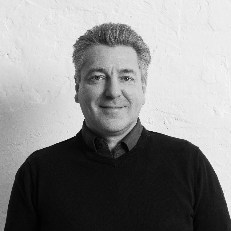 Felix Braun lächelt in einem schwarzen Pullover vor einer weißen Wand.