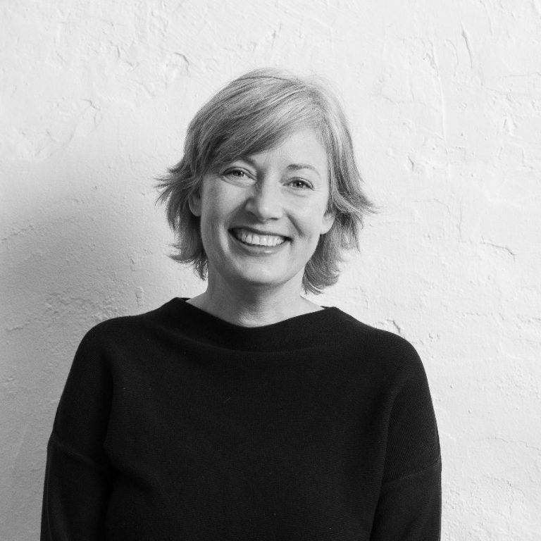 Katrin Schuppelius mit blonden Haaren, trägt einen schwarzen Pullover, vor einer hellen Wand.